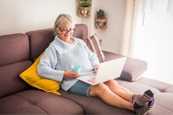 A photo of a white woman with blonde hair lying in bed with a sleep mask on, inserting a device into her ears to mask her tinnitus.